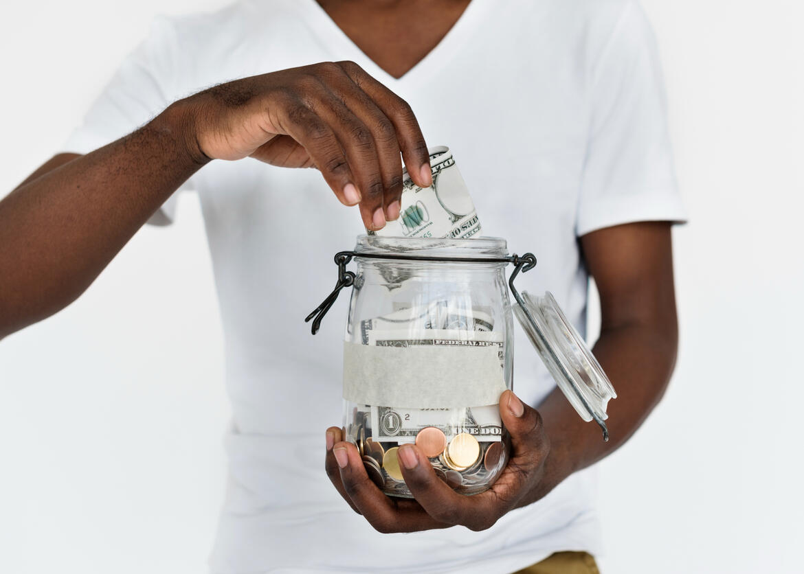 African american male placing cash money in a big mason jar